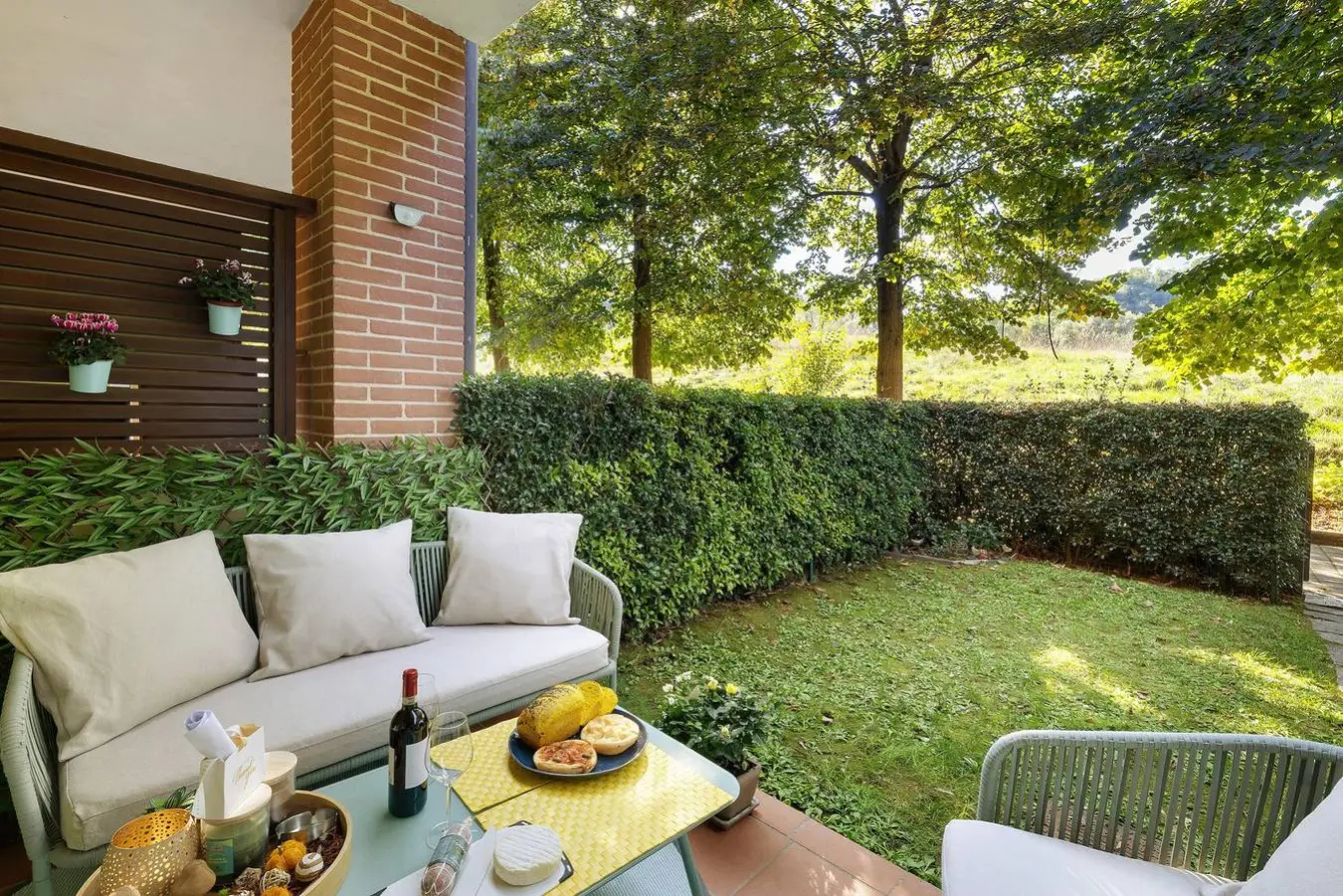 Il patio privato con divanetto e tavolino, davanti al giardino con la siepe